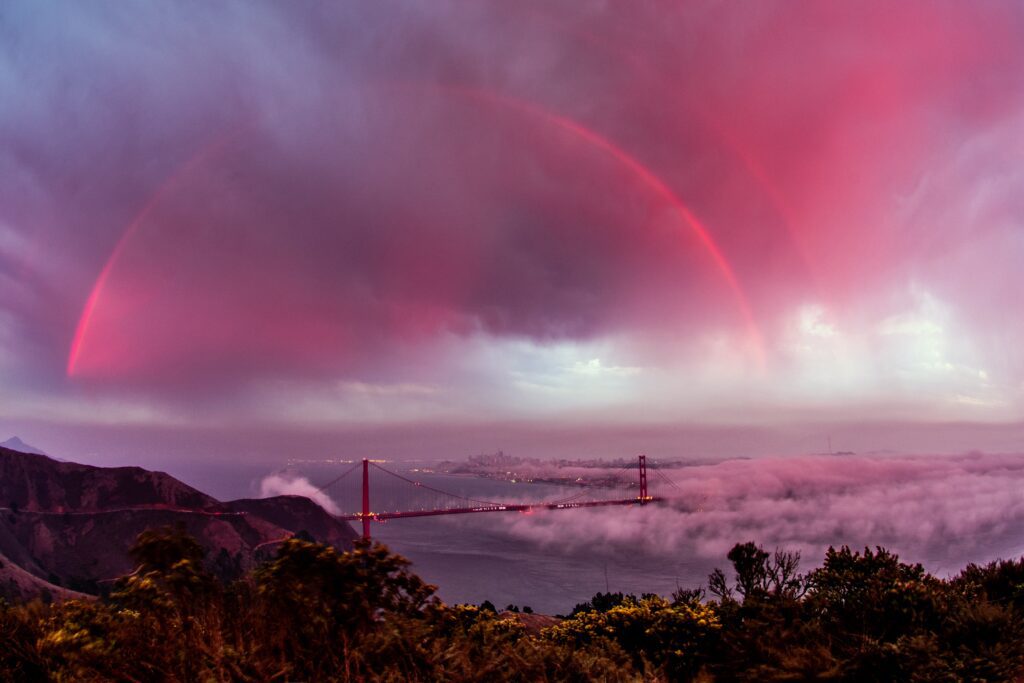 Regenbogen über Golden Gate Bridge in rot. Metapher für die Verbindung von erfahrung eines ersatzkindes und therapeutischer erfahrung, forschung und wissenschaft, aus der großes entstehen kann