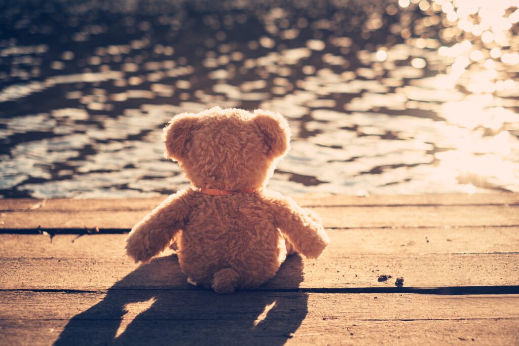 Teddy sitzt auf einem Steg vor einer Wasseroberfläche, in der sich das Licht spiegelt. Auch für Ersatzkinder gibt es Hoffnung, aus der Bindung durch Schuldgefühle zu entkommen. Der Weg beginnt mit Bewusstwerdung und Verantwortungsübernahme.