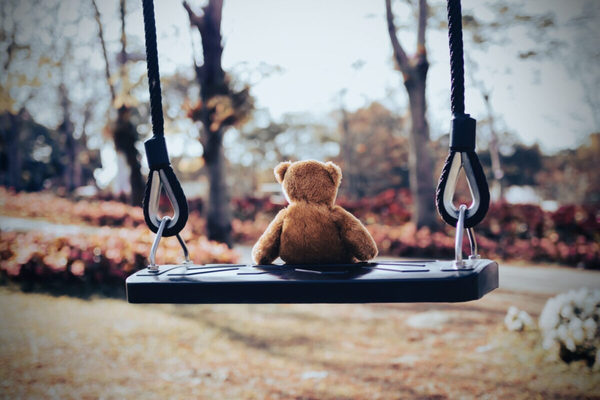 Ein einsamer Teddy in der Rückansicht auf einer Kinderschaukel. Schuld und Schuldgefühle sind bei Ersatzkindern quälender Begleiter ihres ganzen Lebens. Der Artikel handelt von ihrer Entstehung, den Folgen und den Möglichkeiten, sich daraus zu befreien.