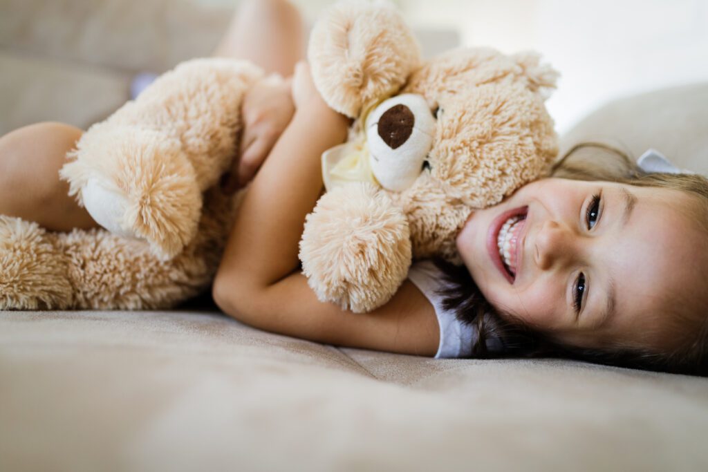 Ein kleines Mädchen umarmt strahlend ihren Teddy. Die Aufgabe von Ersatzkindern ist es, zu verstehen und zu fühlen, dass sie als Mensch gut und liebenswert sind. Die übernommene Schuld ist nur eine Illusion. Die Schuld- und Schamgefühle dürfen geringer werden und irgendwann ganz verschwingen. Das geschieht durch Selbstliebe und Selbstmitgefühl auf dem Weg der Individuation.