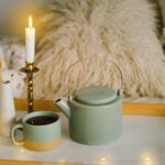 Ein warmes Getränk und eine brennende Kerze vor einem gemütlichen Ambiente. Der Adventskalender für Menschen mit Geschichte soll eine besinnliche Einkehr zu sich selbst werden. Ein Wiedererkennen der eigenen Werte und ein Schritt zu mehr Liebe zu sich selbst.